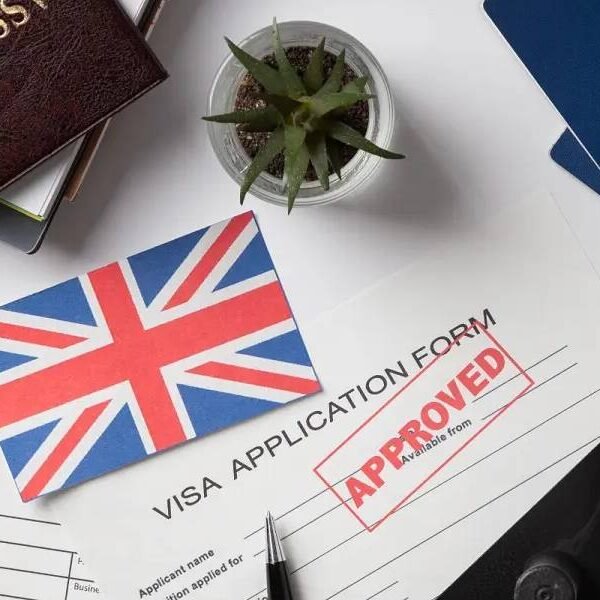 A UK visa application form stamped “APPROVED” with the British flag, passport, and boarding pass on a white desk – symbolizing successful UK visa approval for study or travel.