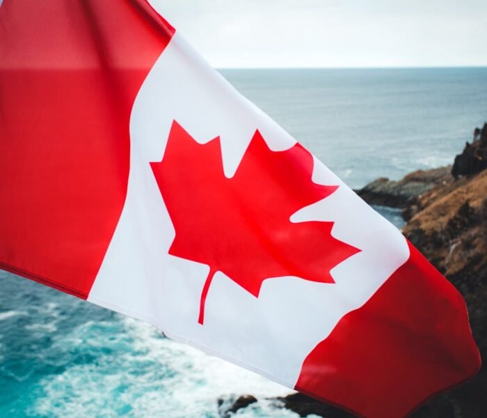 Canadian flag with red maple leaf against coastal cliffs and ocean background – study in Canada with ASK Consultants Karachi.
