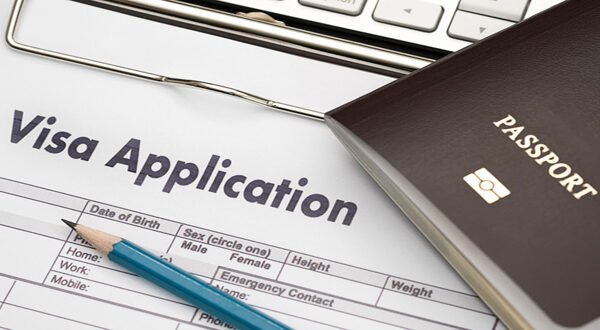 Close-up of a visa application form with passport, pencil, and computer keyboard on a desk, representing the student visa application process and international travel preparation.